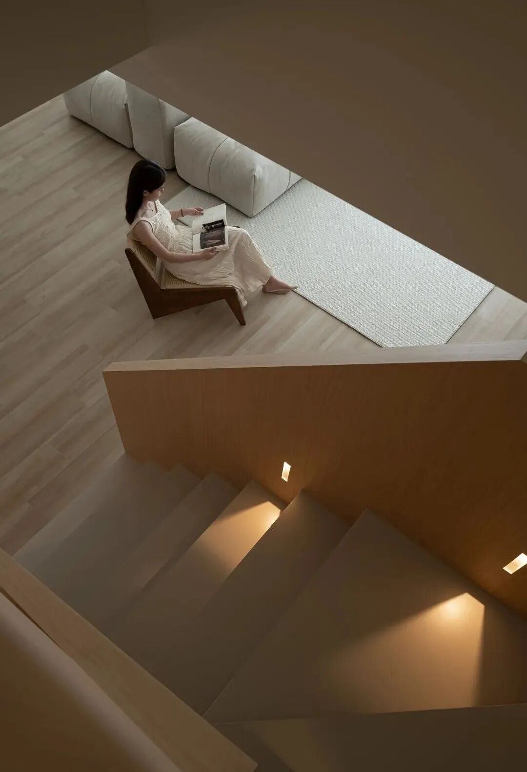 Modern duplex living room with neutral sofa, wooden staircase, and warm ambient lighting